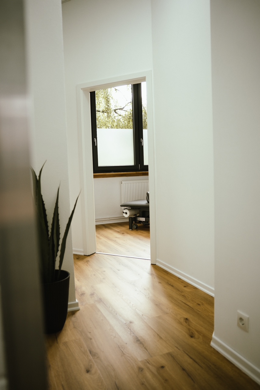 Blick durch den hellen Praxisflur in einen Behandlungsraum
